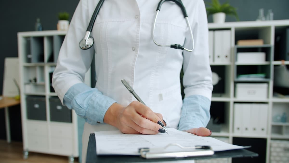 Close-up shot of hand of doctor writing in patient's medical records ticking symptoms working in hospital office. Medicine, paperwork and profession concept.