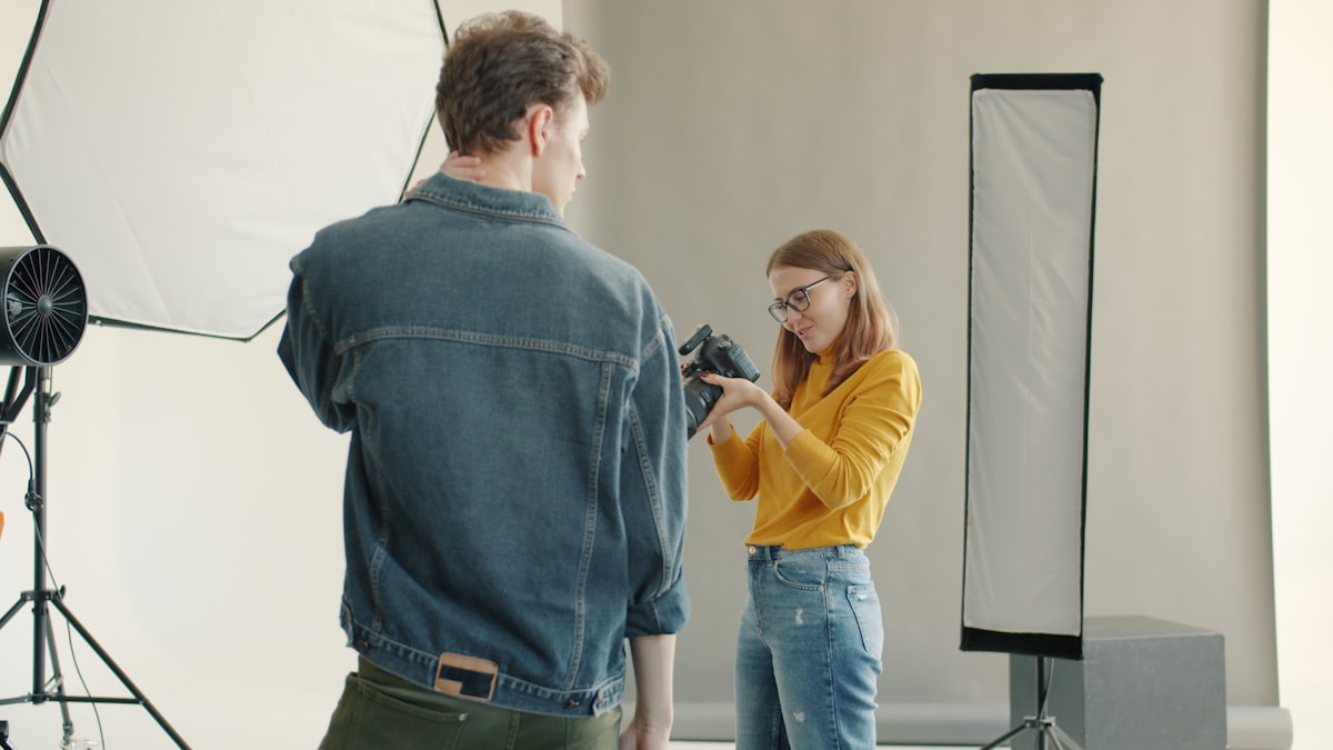 Professional photographer attractive young woman taking pictures of male model using camera in modern studio enjoying work together.